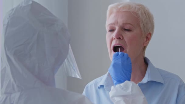 Προσωπογραφία αγνώριστη τεχνικός εργαστηρίου γυναίκα γιατρός σε προστατευτική στολή παίρνει δείγμα από τη γιαγιά ασθενή ηλικιωμένη καυκάσια γυναίκα ηλικιωμένη κυρία για τον ιό coronavirus covid-19 στο σπίτι, νοσηλεύτρια σε εσωτερικούς χώρους — Αρχείο Βίντεο