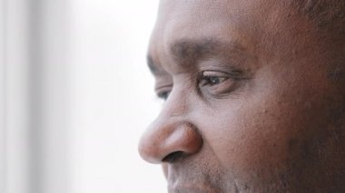 Aşırı yüz hatları, olgun Afrikalı orta yaşlı adam, kırışıklıkları olan, pencereden dışarı bakan, hayal kuran, başarılı bir lazer düzeltme operasyonundan sonra iyi görüşün tadını çıkaran 50 'li yaşlarda erkek gözleri.