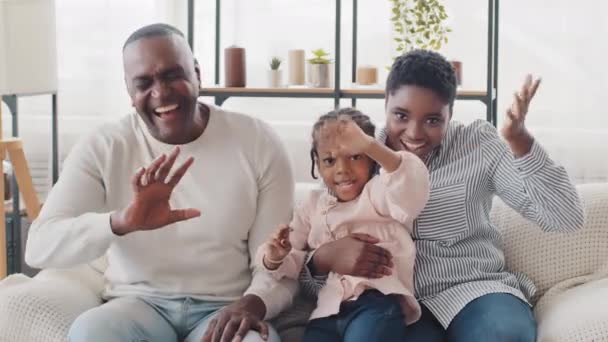 Africano afro família feliz pais e pequena menina criança negra sentado em casa sofá rindo em voz alta sinceramente sorridente dentário acenando Olá saudações posando na acolhedora sala de estar, chamada de vídeo — Vídeo de Stock