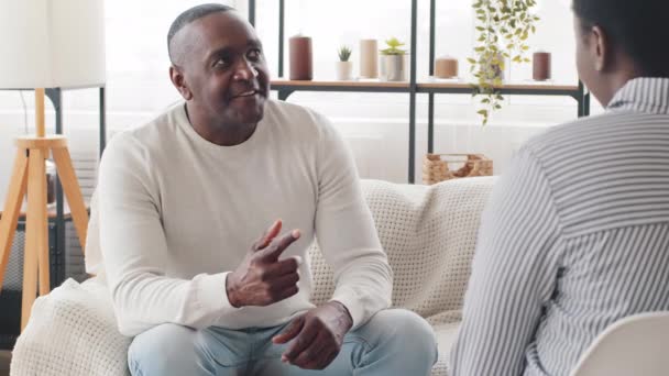 非洲男人成熟的黑人男女混血患者在与心理医生谈话时，有心理问题坐在沙发上，依靠手指与无法辨认的女性专家进行咨询 — 图库视频影像