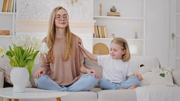 Kafkasyalı, genç, sakin anne, sarışın, yeni yürümeye başlayan kızla meditasyon yapıyor. Kız çocuğu koltukta oturuyor. Küçük çocuk gürültü yapıyor. — Stok video