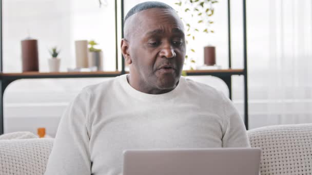 Maduro sênior africano americano homem preto mestiço étnico masculino usuário sentado em casa no sofá usando laptop moderno para o trabalho leitura notícias navegação bate-papo compras on-line, pessoas idosas e tecnologia — Vídeo de Stock
