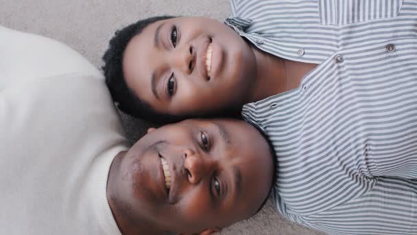 Top melihat pasangan Afrika menikah pria dan wanita tergeletak di lantai dalam rumah baru melihat kamera. Shooting from above ethnic black afro heads wife and husband people in love tottish — Stok Video