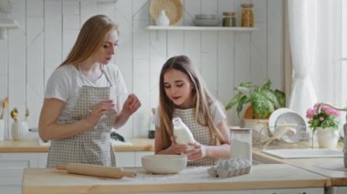 Yetişkin anne, beyaz kadın ev hanımı, küçük kız çocuğuna yemek pişirmede yardım etmeyi öğretiyor. Küçük çocuk, bovling oynamak için süt katıyor, evde birlikte yemek pişiriyorlar, kolay öğreniyorlar.