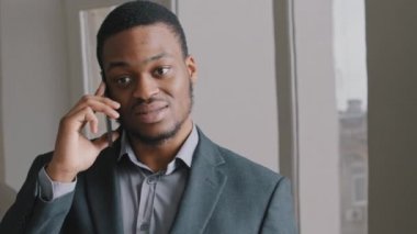 Genç Afrikalı erkek yönetici cep telefonuyla konuşuyor. Ofiste cep telefonuyla iş görüşmesi yapıyor. Ciddi etnik adam müşteriyle konuşuyor. Sorunları cep telefonuyla çözüyorlar..