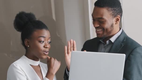 Glad smilende ung afrikaner amerikansk forretningskvinde forretningsmand professionel ved hjælp af bærbar computer på arbejdspladsen, der arbejder online på notesbog i moderne kontorrum giver high five fejrer sejr – Stock-video