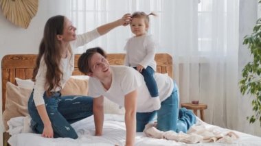Kafkasyalı mutlu aile hafta sonunu yatakta birlikte geçirir. Neşeli baba, küçük kızı sırtında taşır. Küçük kız çocuğuyla oynar.