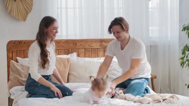 Little girl baby toddler infant daughter falls on soft bed young caucasian mother laughs caring father cuddle kid, happy family relaxing playing in bedroom enjoying love time bonding weekend at home — Stock Video