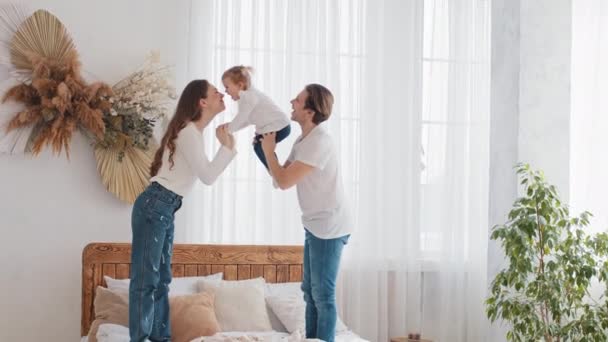 Kaukasische zorgzame vader sterke vader houden baby in de armen verhoogt lift kleine dochter in de lucht, jonge moeder liefdevolle moeder spreekt met kind spelen touch handen, familie brengt tijd samen thuis in gezellige slaapkamer — Stockvideo