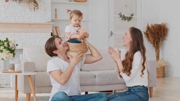 Kavkazská rodina baví doma hrát hru s malou dcerou bezstarostný silný otec zvedá dítě drží malou dívku na rameni dítě sedí v proutěný koš dítě česání mamina vlasy pomocí hřeben — Stock video