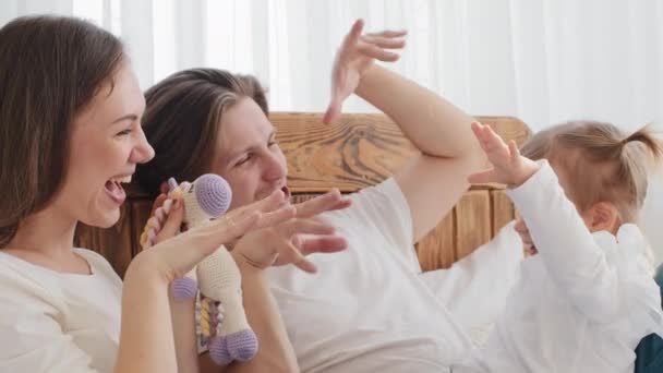 Feliz família caucasiana jovens pais milenares pai amoroso e mãe carinhosa brincar com a filha pequena bebê segurar macio de malha unicórnio brinquedo cócegas criança criança criança rir desfrutar de ligação em casa — Vídeo de Stock