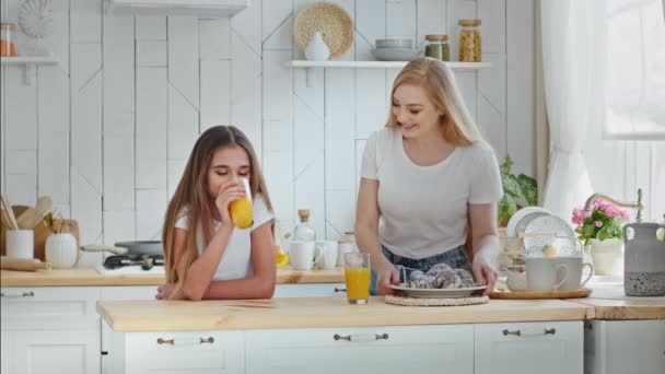 Älskade omtänksam mor hemmafru sätter tallrik hemmagjorda kakor på köksbordet kramar kramar omfamna älskad dotter tonåring flicka barn dricka apelsin tropisk färsk juice njuter bindning kärlek — Stockvideo