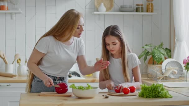 Blanke moeder huisvrouw leert tiener dochter schoolmeisje kind toont hoe om groenten te snijden rode tomaten bereiden verse vegetarische salade, familie koken lunch diner in de keuken thuis samen — Stockvideo