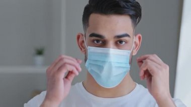 Beyaz tişörtlü Arap bir adamın portresi. Mavi koruyucu maskeyi çıkartıyor. Yüzünden nefes alıyor. Kapalı yerde durup Coronavirus salgını salgını sona eriyor.