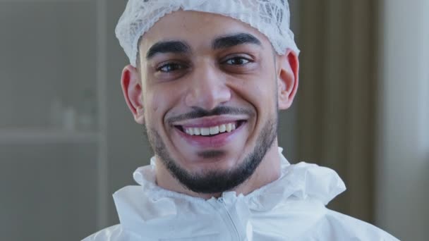 Glimlachende arts Arabische chirurg Spaanse verpleegkundige medisch medewerker in speciale uniform hoed kijkt naar camera glimlach tand na succesvolle operatie werken met coronavirus genieten einde van covid-19 pandemie — Stockvideo
