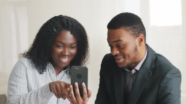 Lenyűgözött boldog afrikai üzletasszony bemutatja okostelefon képernyőn, hogy a fiatal férfi kolléga üzletember. Izgatott örömteli különböző kollégák olvasás jó hír úgy érzi, elégedett mutató kéz gesztus oké — Stock videók