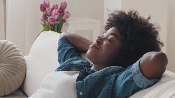Здоровая уставшая безмятежная афроамериканская молодая женщина, опирающаяся на удобный диван, делает массаж шеи. Спокойная черная леди расслабляется на уютном диване, не наслаждаясь стресс-концепция дома, близко вверх ногами вид — стоковое видео
