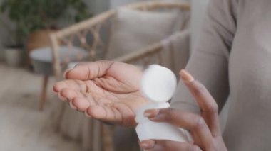 İlaç şişesinden hap dolduran Afrikalı genç bir bayan ağrı kesici kapsülleri tutuyor. Ağrıyı dindirmek için ilaç alıyor. Hasta ruhlu, yetişkin kadın sağlık hizmetleri, eczane ilaç konsepti, yakın çekim.