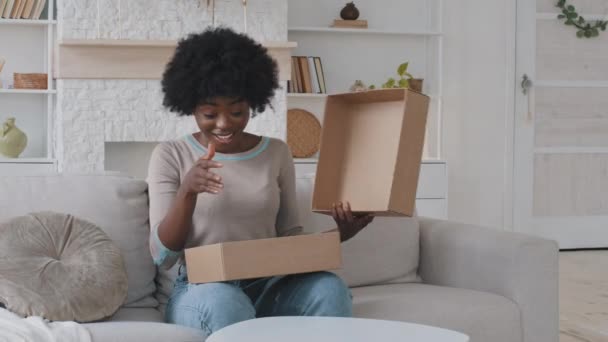 Emocionada joven mujer de raza mixta abriendo la caja de paquetes en casa. Sorprendido mujer feliz consumidor chica shopper unboxing compra de moda sentado en el sofá recibir paquete de cartón con regalo inesperado — Vídeos de Stock