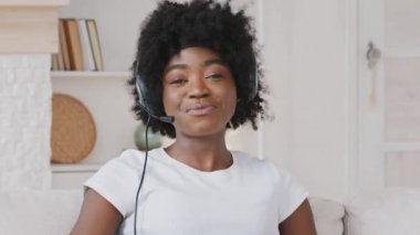 Gülümseyen Afrikalı genç bir kadın web kamerasına kulaklık takıyor ve uzaktan video konferans görüşmesi yapıyor. Bayan internet öğretmeni evden uzakta sohbet ediyor. Telework konsepti. Web kamerası görünümü