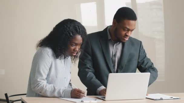 Young experienced african male mentor coach teaching instructing young female intern. Trainee new worker making notes explaining new project looking at laptop computer at apprentice course in office — Vídeo de stock