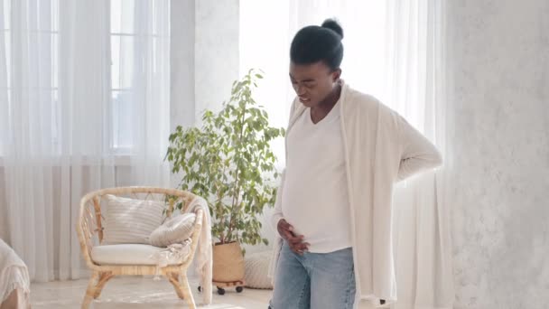 Молода афроамериканка вагітна жінка, яка тримає животик, сподіваючись, що майбутня мама кричатиме від болю немовляти, турботливий батько африканського африканця обіймає чоловіка і підтримує дружину вдома. — стокове відео