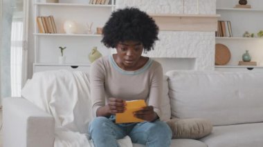 Upset African American ethnic girl feel frustrated open envelope at home reading bad news receive paper post mail letter about financial problem, bank debt bill, failed exam test results or subpoena