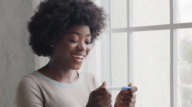 Happy attractive emotional African young lady hold pregnancy test great surprised positive result, overjoyed mixed race female adult feel excited expect baby after IVF fertility treatment concept