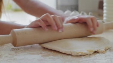 Ev mutfağındaki merdaneyi kullanarak un hamurunda yuvarlanan çocuğun yakın plan fotoğrafı. Tanınmayan kız, pişirmeye yardım ediyor. Pasta hazırlıyor. Masada yumurta ve süt var..
