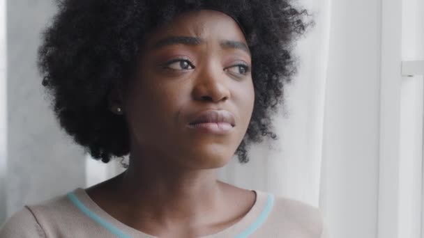 忧心忡忡的绝望的年轻的非洲裔美国忧郁女人从家里的窗户向外望去，感到悲伤或沮丧。困难关系首先是没有回报的爱情心理情感障碍的概念 — 图库视频影像