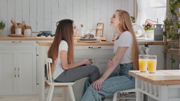 Kaukasisk mor mor babysitter taler til teenage pige barn datter sidder i køkkenet hjem i nærheden af bordet med to briller appelsinjuice deler følelser taler afslappet samtale griner – Stock-video