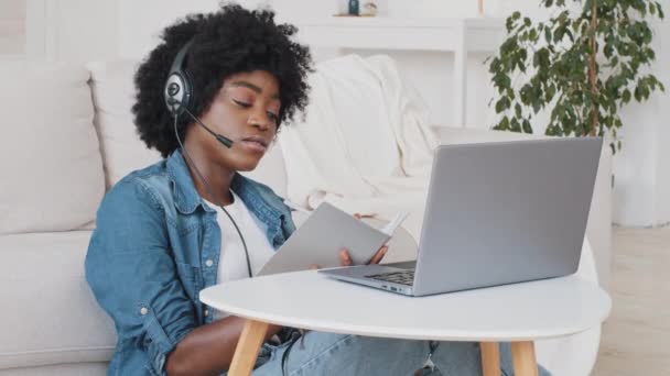 Genç Afro-Amerikalı akıllı kız öğrenci web kamerasıyla e-öğrenim kulaklığı takıyor. Ciddi odaklı milenyum kadın video konferansı dizüstü bilgisayardan not alıyor. Uzaklık eğitimi kavramı — Stok video