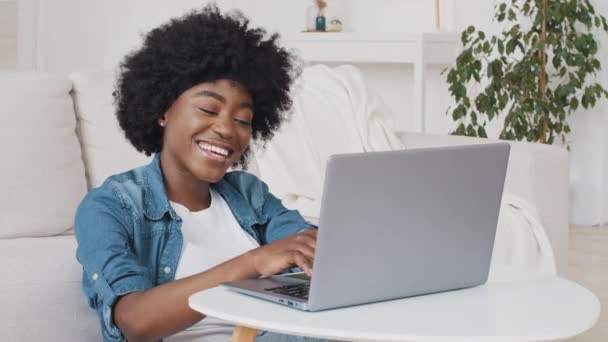 Jovem afro-americana feliz fazer trabalho remoto em casa na mesa sorriso desfrutar de atividade teletrabalho. Lady passar o tempo conversando em redes sociais usar laptop, procurar informações úteis para o trabalho ou estudo — Vídeo de Stock