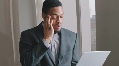 Yorgun, genç, Afrikalı, melez, profesyonel işadamı öğrenci ofis bilgisayarlarında çalışırken yoruluyor viski masajı yapıyor, esniyor. Çok çalışan erkek işkolik çok yoruldu.