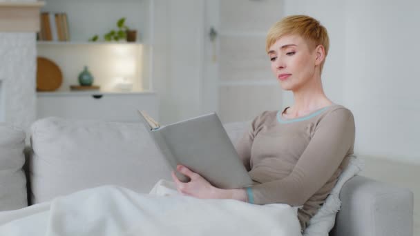 Femme rêveuse relaxante tenant lecture de livre assis sur le canapé, réfléchit sur la lecture, réfléchit en regardant au loin, profiter d'un week-end confortable et paresseux à la maison. passe-temps favori, littérature, éducation, nouveau concept de connaissance — Video