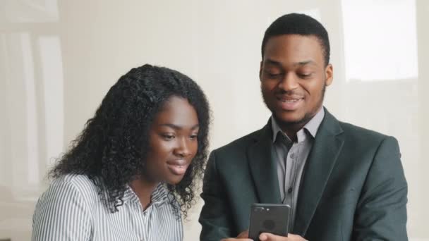 Glückliches Millennial-Paar plaudert lachend über Smartphone mit lustigen Apps in Coworking lächelnd Mann und Frau entspannt im Büro Spaß in den sozialen Medien auf dem Handy online anschauen Video auf dem Handy — Stockvideo