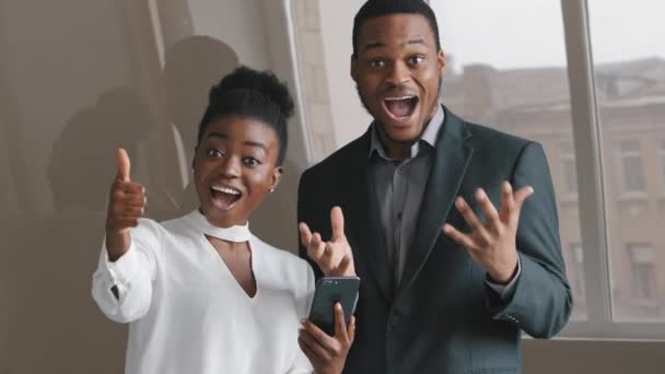 Emotioneel blij vrolijke jonge Afrikaanse etnische collega 's kijken naar het telefoonscherm, lachen enthousiast over het krijgen van bericht met geweldig nieuws, vieren online loterij winnen tonen duimen omhoog — Stockvideo