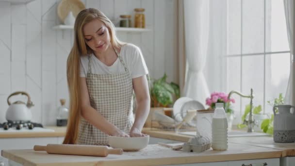 Mujer caucásica con el pelo largo ama de casa adulta panadero mujer cocina lleva delantal se para en la cocina casera moderna prepara amasar masa con harina huevos y leche pastel de cocina galletas caseras pastel cena almuerzo — Vídeo de stock