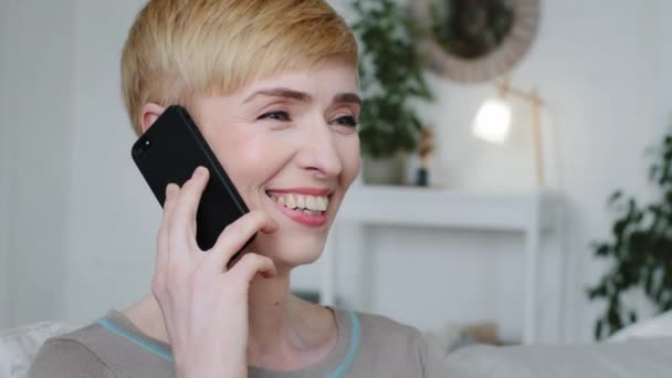 Headshot portret mooie dame zitten in de moderne woonkamer praten op Mobiele telefoon ontvangen overleg op afstand, orde op afstand. Jonge vrouw met behulp van smartphone hebben aangename persoonlijke gesprek — Stockvideo