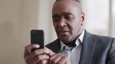 Konsantre olmuş yetişkin Afro-Amerikan iş adamı etnik siyahi lider ciddi bir ifadeyle telefon ekranına bakıyor dokunmatik hat hattındaki web tuşlarına cep telefonu kullanarak bakıyor.