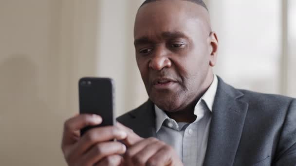 Concentré mûr homme d'affaires afro-américain mûr chef ethnique noir avec une expression sérieuse regarde l'écran du téléphone navigue sur les clics Web sur le pavé tactile cadrans de chat en utilisant smartphone gadget mobile — Video