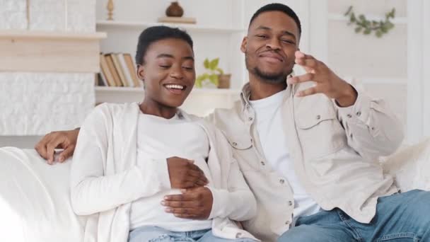 Retrato afro-americano embarazada pareja negra étnica familia futuros padres sentados en el sofá en la sala de estar cantando canción disfrutando del embarazo y la música bailando hablando por videollamada en línea conferencia chat — Vídeos de Stock