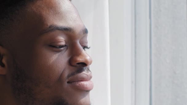 Retrato inspirado homem africano feliz sentindo harmonia olhando para a janela em casa sonhando pensar sobre planos futuros apreciando a vista da cidade pôr do sol do sol fora, close-up cara étnica masculina negra — Vídeo de Stock