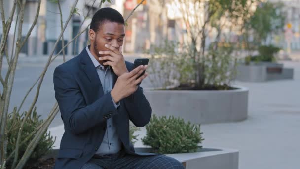 Millennial hombre de negocios negro usuario de tecnología móvil que trabaja en aplicaciones digitales gadget búsqueda de información en línea, mensajes de texto. Sonriendo joven hombre afroamericano utilizando el teléfono inteligente al aire libre — Vídeos de Stock