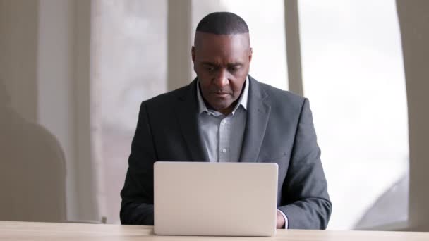Концентрированные серьезные занят зрелый молодой африканский бизнесмен среднего возраста афро-босс лидер черный мужчина работник носит официальный костюм использует ноутбук для работы в офисе за столом просмотра сети в компьютере — стоковое видео