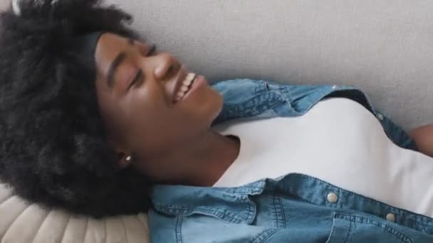 Souriant serein détendu jeune fille adulte repos couché sur un canapé confortable, calme heureuse femme afro-américaine détendre les yeux fermés sieste sur le canapé dans le salon profiter se sentir salon sans stress à la maison — Video
