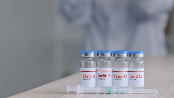 Close-up of four jars bottles with covid-19 vaccine stand on wooden table in clinic near syringe unrecognizable woman scientist doctor nurse medical worker takes one dose of coronavirus medicine drug — Αρχείο Βίντεο