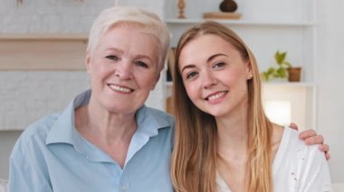 Happy dreamy beautiful 2 two age generations women looking away at camera. Loving mature older mother hugging happy young adult grown daughter. Family enjoys sincere emotions tenderness mothers love