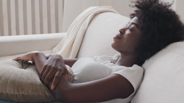 Gros plan de mixte jeune femme se détendre appuyé sur un canapé confortable dans la lumière chaleureuse salon confortable seul, se sent heureux, profiter appartement loué, week-end dans un appartement moderne climatisé, concept sans stress — Video