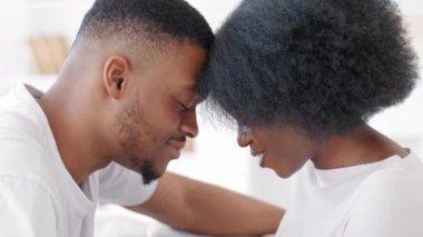 Afro american married couple in love ethnic black newlyweds spouses boyfriend and girlfriend millennial man and curly woman sitting on sofa at home indoors touching foreheads enjoying intimacy bonding